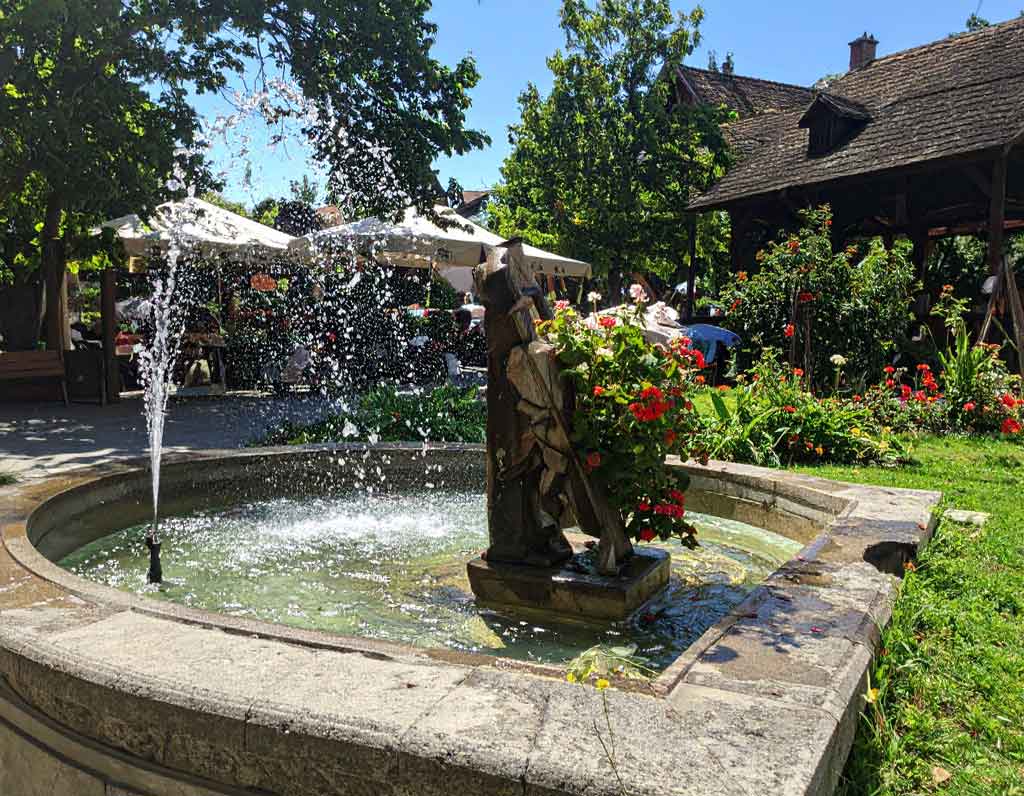 Ein idyllisches Garten-Café mit plätscherndem Steinbrunnen, umgeben von bunten Blumen — ein inspirierender Ort für entspannte Gespräche und zum Englisch lernen in natürlicher Atmosphäre.