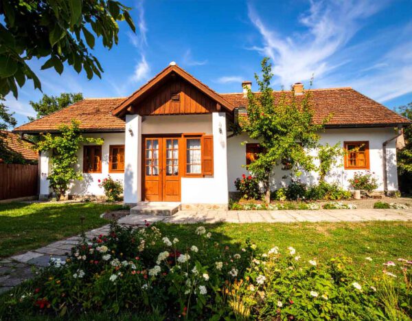 Charmantes ungarisches Landhaus mit weißer Fassade, braunem Ziegeldach und blühendem Garten symbolisiert einen sonnigen Tag in Csepreg, Komitat Vas