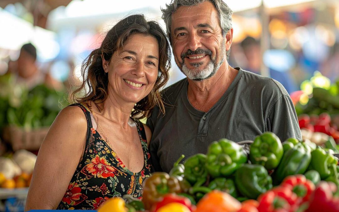 Lächelndes Paar auf einem bunten Wochenmarkt in Ungarn, umgeben von frischem Gemüse wie Paprika und Tomaten. Ein Moment voller Lebensfreude, Gemeinschaft und regionaler Verbundenheit – so fühlt sich Auswandern nach Ungarn wirklich an.