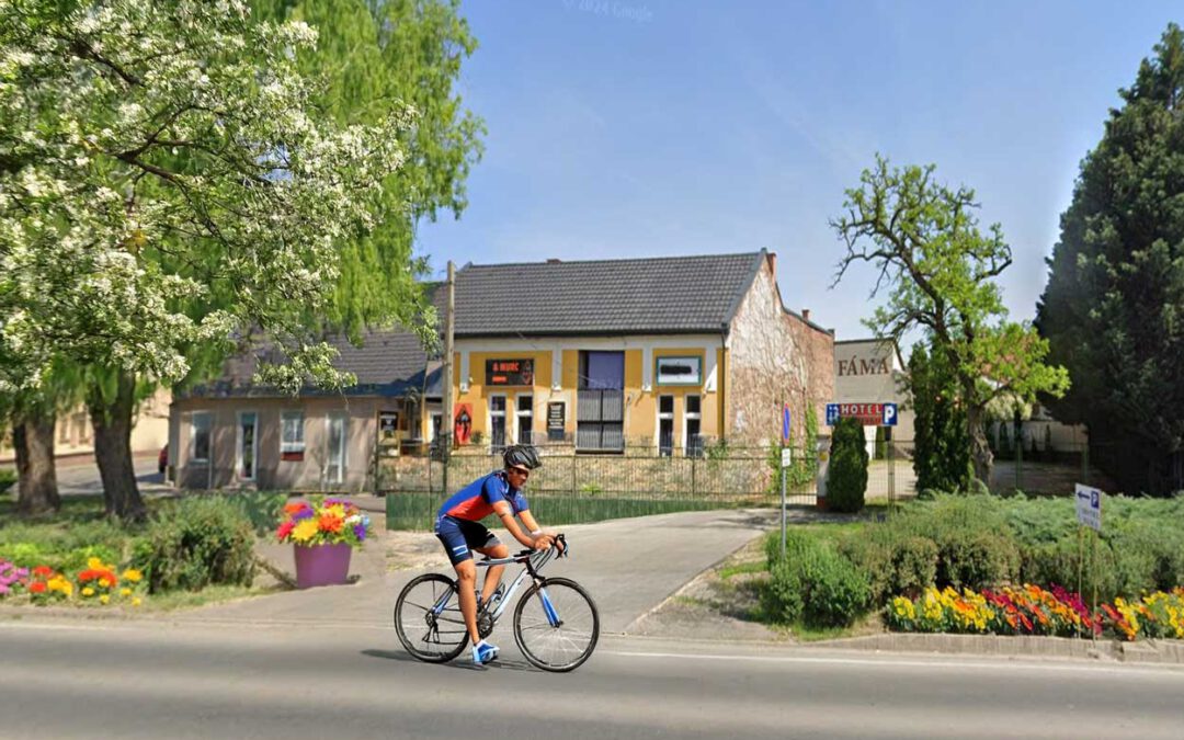 Radfahrer vor kleinem Hotel und Blumenbeeten in Hodmezovasarhely – sonniger Straßenzug, ruhiger Alltag in Ungarn, passend zum Thema Auswandern.