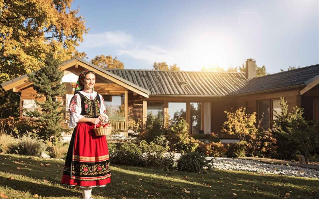 Ungarische Frau in traditioneller Tracht steht vor einem Haus in Sandorfalva im Komitat Csongrad-Csanad – Symbolbild fuer Auswandern nach Ungarn, Rentnerleben und Lebensqualitaet