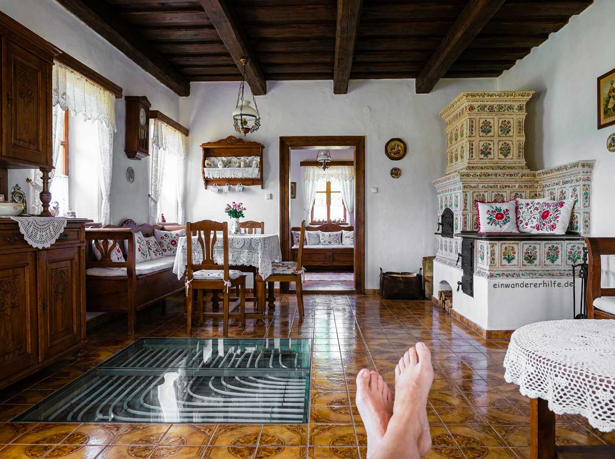 Traditionelles ungarisches Dorfhaus mit sichtbar integrierter Fußbodenheizung unter den Fliesen; Wohnraum mit Kachelofen, Holzdecke und dekorierten Möbeln. Darstellung der modernen Heiztechnik im Altbau – passend zum Thema Stromkosten in Ungarn und effiziente Fußbodenheizung.
