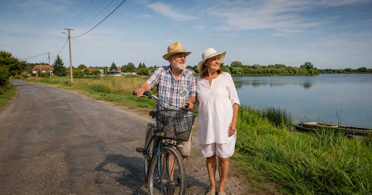 Glückliches Paar am See in Jász-Nagykun-Szolnok in Ungarn mit Fahrrad, ländlicher Straße, Stromkabeln in der Luft und naturnaher, heller Sommerstimmung
